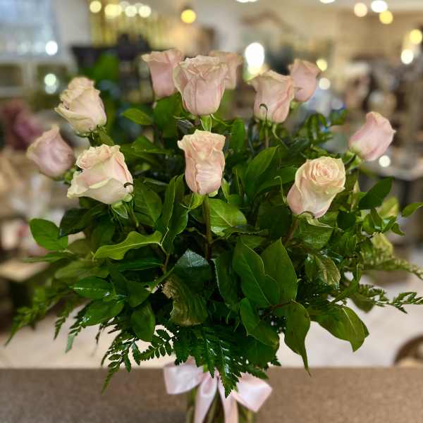 Bouquet of pale pink roses in a clear glass vase with a pink ribbon