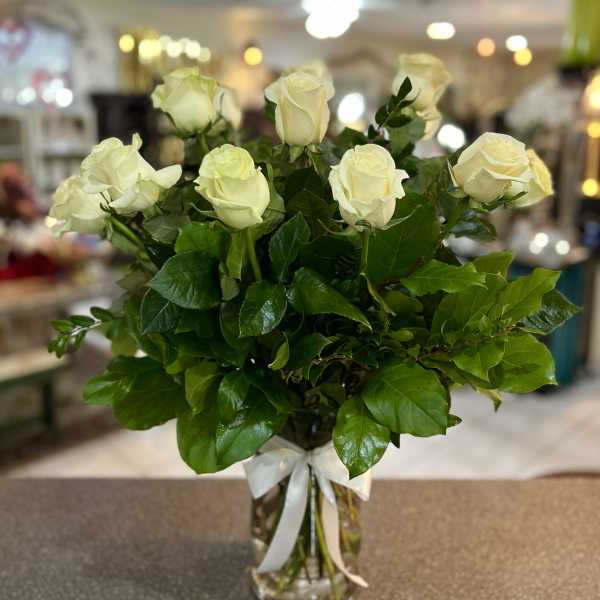 White roses arranged in a clear glass vase with a white ribbon