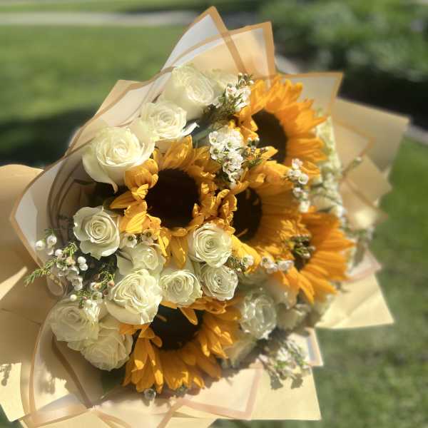 Bouquet of white roses and sunflowers wrapped in tan paper