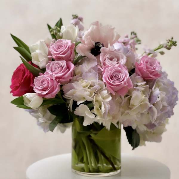 Pink roses, white tulips, anemones, and pastel hydrangeas in a clear glass vase