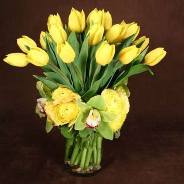Yellow tulips and roses arranged in a clear glass vase