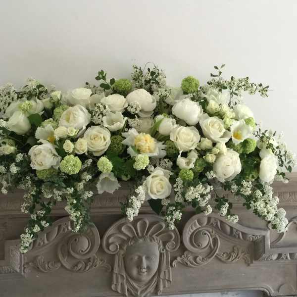 White floral arrangement with roses and peonies on an ornate mantel