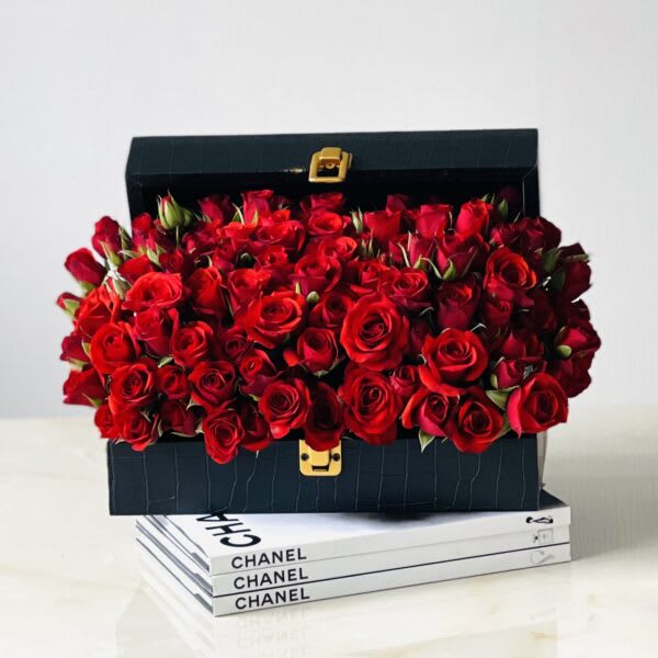 Black box filled with red roses on stacked Chanel books