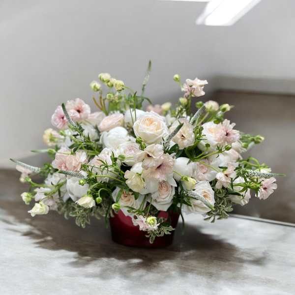 Low floral arrangement of white and blush blooms in a red container