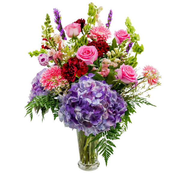 Mixed bouquet of pink roses, purple hydrangea, and red blooms in a glass vase
