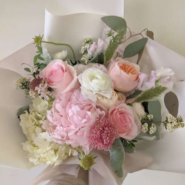 Hand-tied bouquet of pink and white flowers wrapped in pale paper