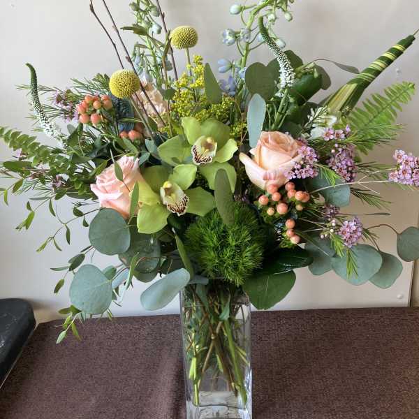Tall mixed bouquet in a clear glass vase with pink roses and green orchids
