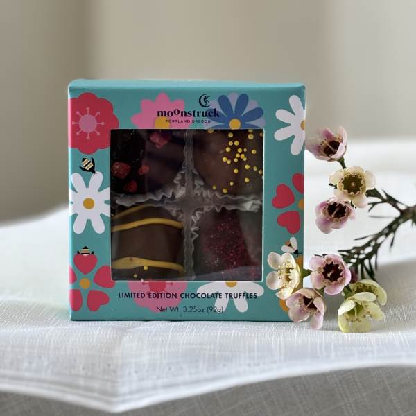 Box of chocolate truffles beside a small sprig of pink and white flowers