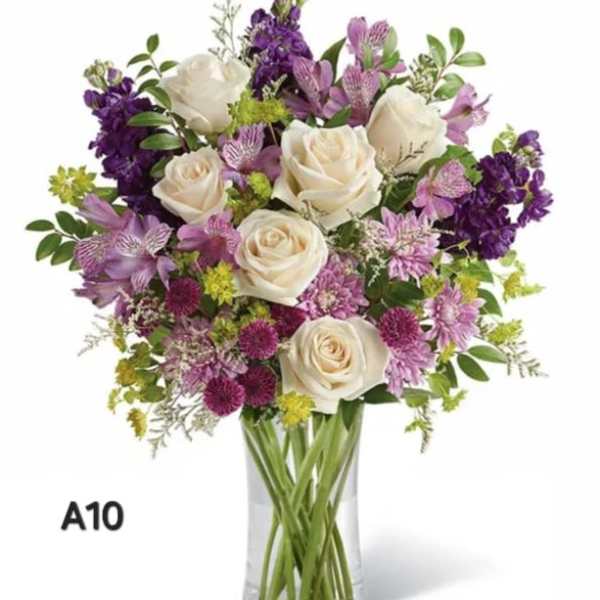 Bouquet of white roses and purple flowers in a clear glass vase