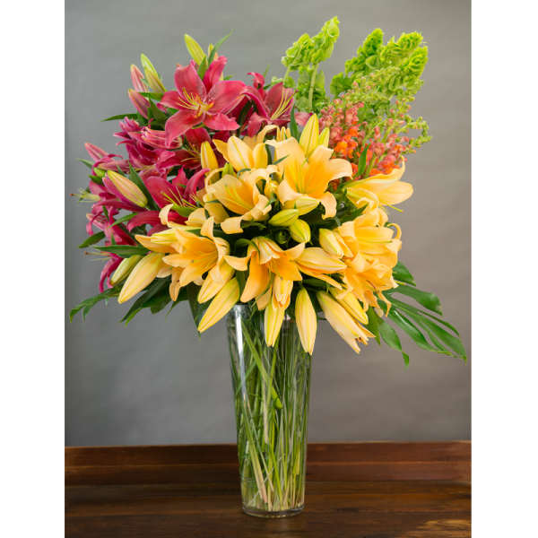 Tall vase arrangement of yellow and pink lilies