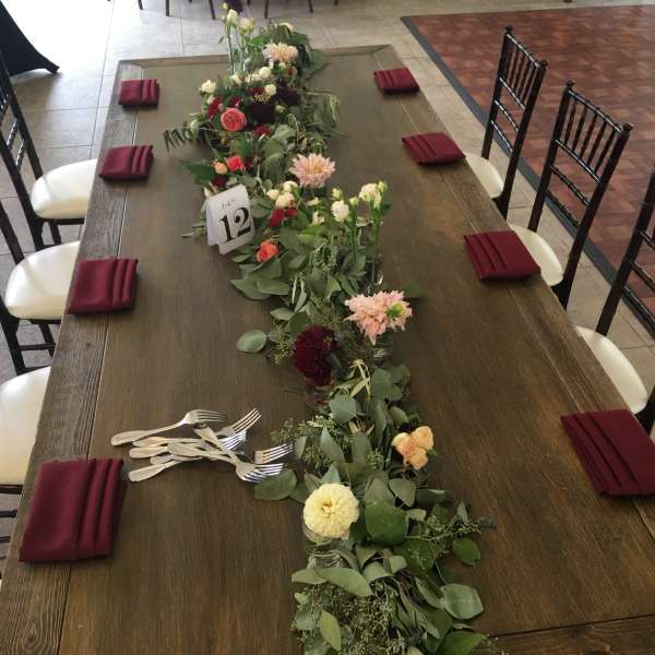 Long floral garland centerpiece on a dining table with small glass vases