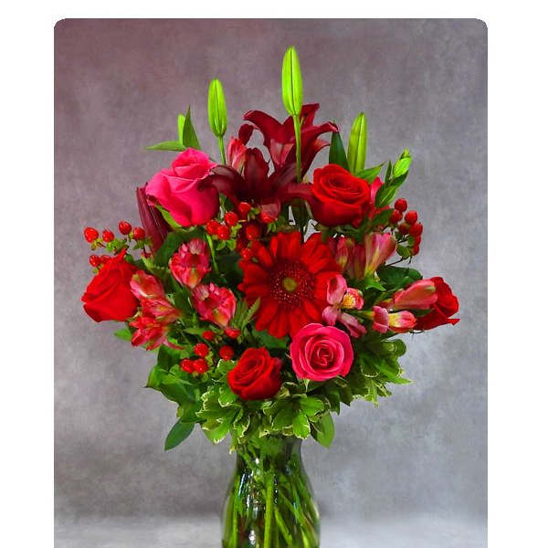 Tall arrangement of red and pink roses, lilies, and gerbera daisies in a clear glass vase