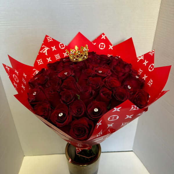 Bouquet of deep red roses wrapped in red patterned paper with a small crown topper