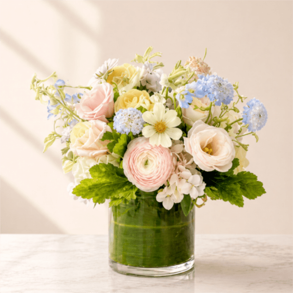 Pastel bouquet of roses, ranunculus, and blue blooms in a glass vase