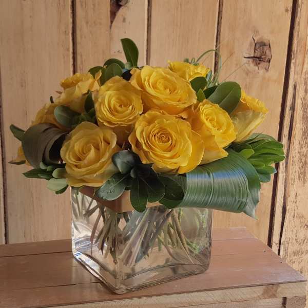 Yellow roses arranged in a clear square glass vase