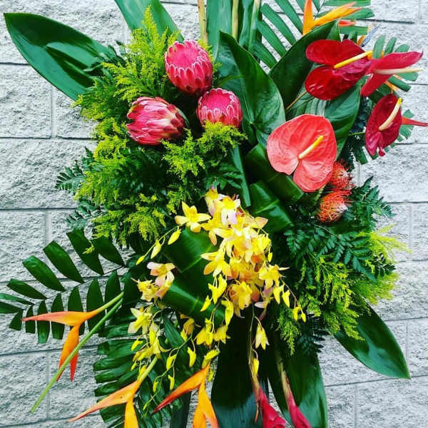 Tropical floral arrangement with red anthuriums, pink protea, and yellow orchids