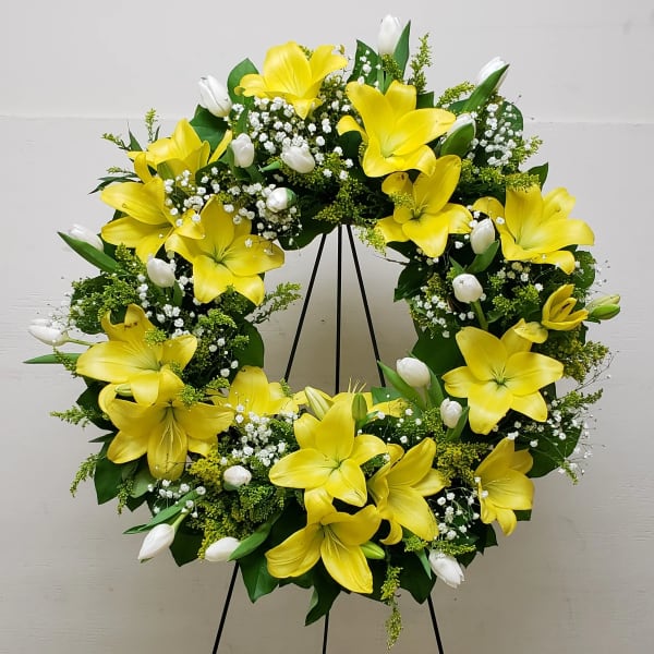 Standing wreath of yellow lilies and white tulips arranged in a ring on a metal easel