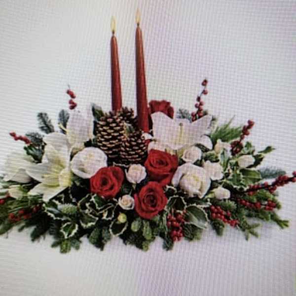 Holiday centerpiece with red and white flowers, pinecones, and two tall candles