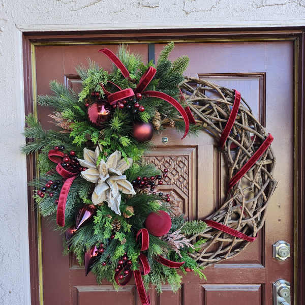 Holiday wreath with evergreen branches, red ribbons, and ornaments on a front door
