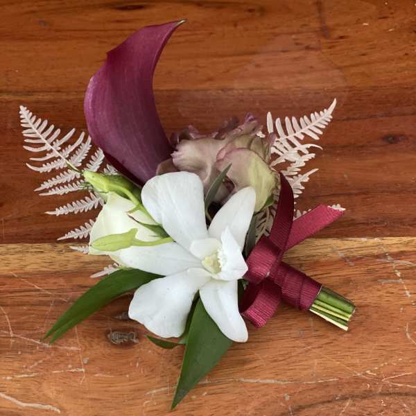 Small boutonniere with white and purple flowers tied with a burgundy ribbon
