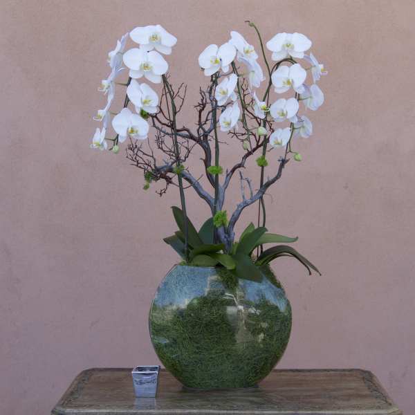 White orchid arrangement in a round green glass vase with a small candle holder beside it