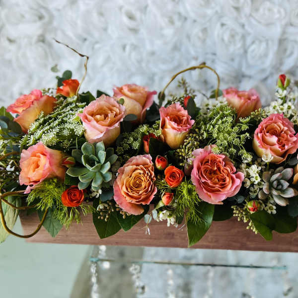 Long low floral arrangement with pink and orange roses in a wooden box