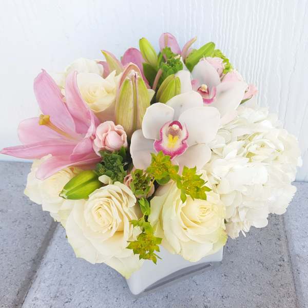 Bouquet of pink lilies, white roses, and white orchids in a white vase