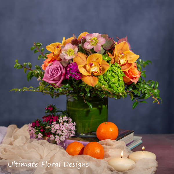 Mixed floral arrangement in a green vase with oranges and candles