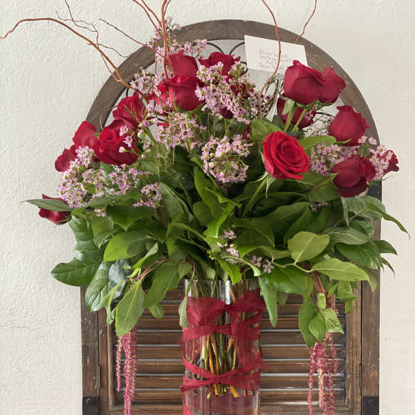 Red roses and pink filler flowers in a tall glass vase with ribbon