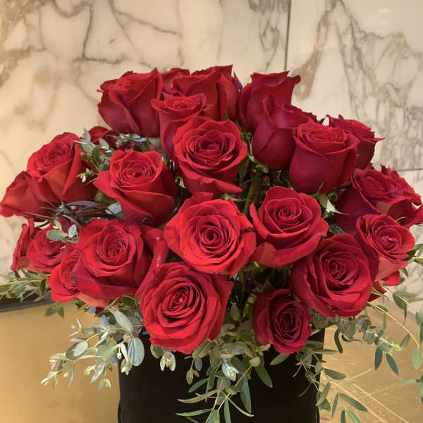 Red roses arranged in a black round box with trailing greenery