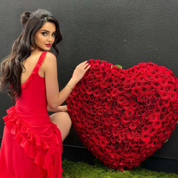 Woman in a red dress posing beside a large heart-shaped rose arrangement