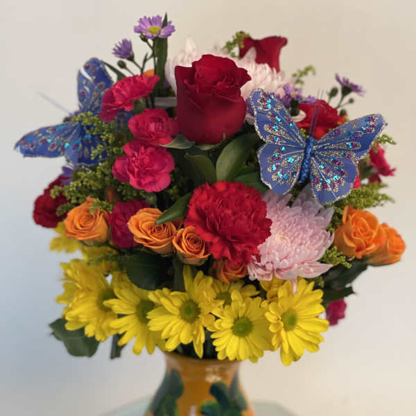 Mixed bouquet of roses, carnations, and daisies in a painted vase with butterfly picks
