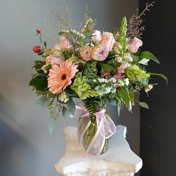 Mixed pink and peach bouquet in a glass vase with a pink ribbon.