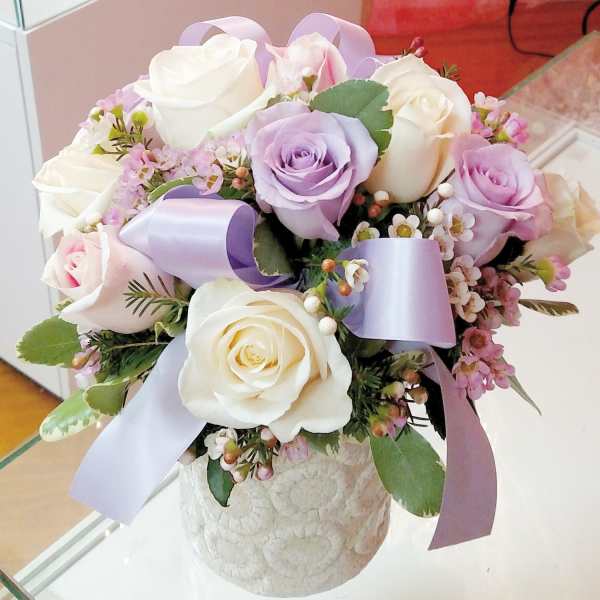 Bouquet of white and lavender roses with lilac ribbon in a textured vase