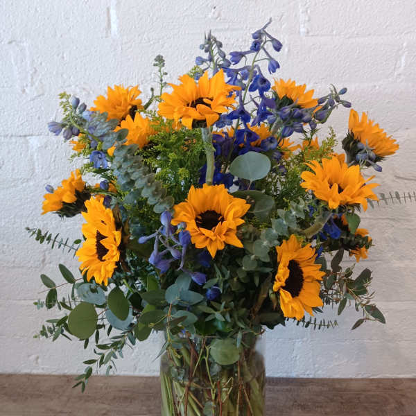 Sunflowers and blue flowers in a clear glass vase