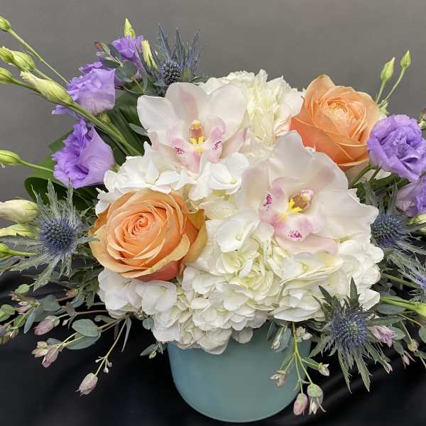 Bouquet of white hydrangeas, peach roses, and purple flowers in a blue vase