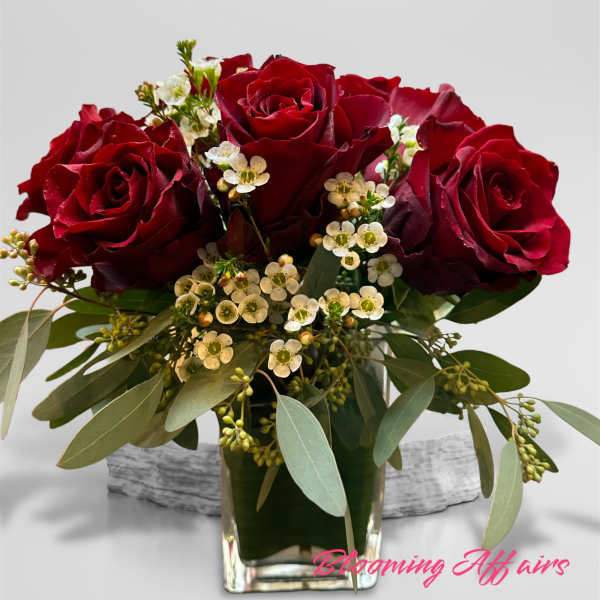 Red roses arranged in a clear glass vase with small white filler flowers