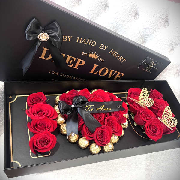 Red roses arranged in a black gift box with gold chocolates and ribbon