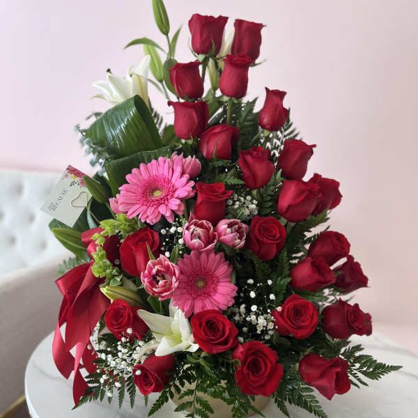 Bouquet of red roses, pink gerberas, and white lilies with a red ribbon