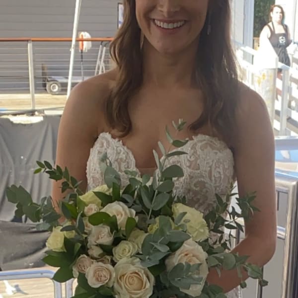 Bride holding a hand-tied bouquet of ivory roses with abundant greenery