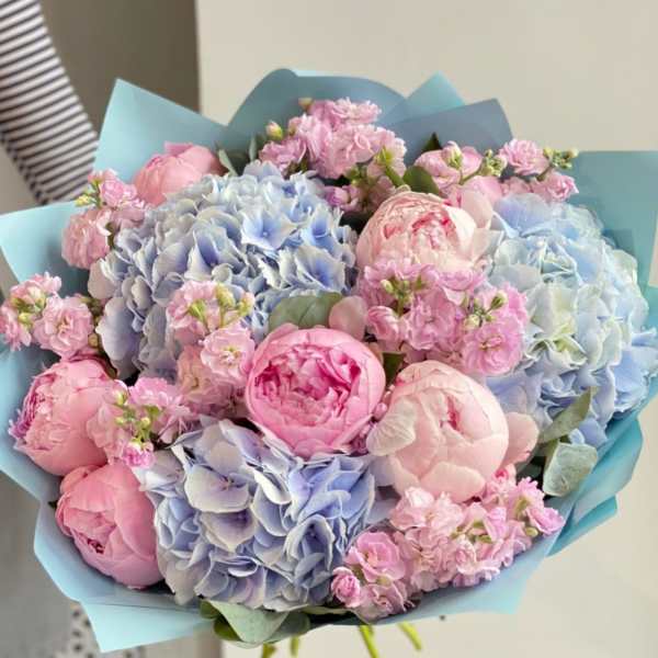Bouquet of pink peonies and blue hydrangeas wrapped in light blue paper