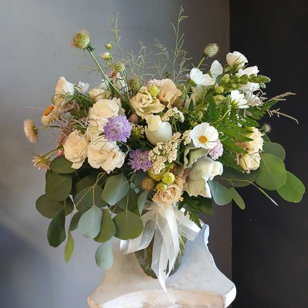 Loose bouquet of cream and white flowers in a glass vase with a white ribbon.