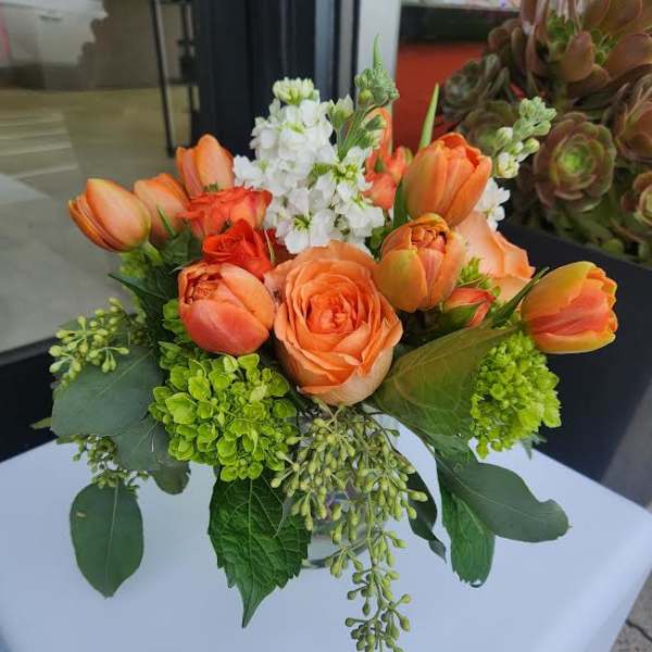 Compact orange rose and tulip arrangement with white blooms in a clear glass vase