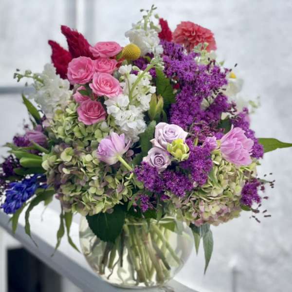 Mixed bouquet of pink, purple, white, and blue flowers in a clear glass vase