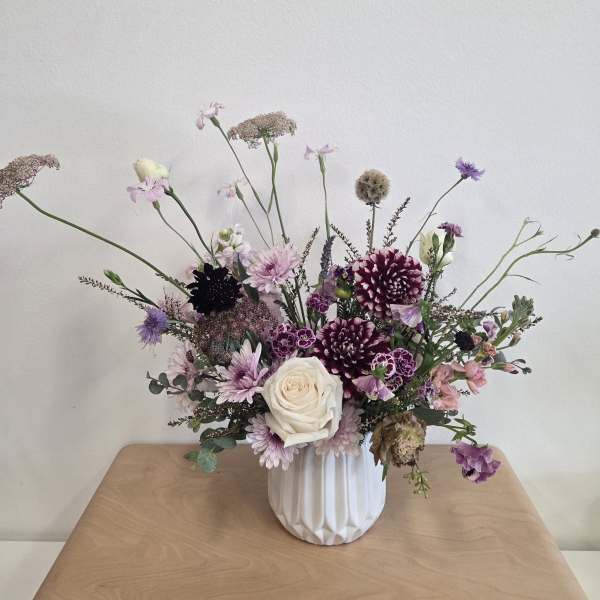 Mixed purple and white floral arrangement in a white vase