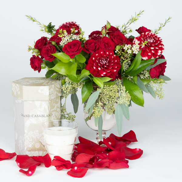 Red roses and red-white dahlias in a glass vase with rose petals