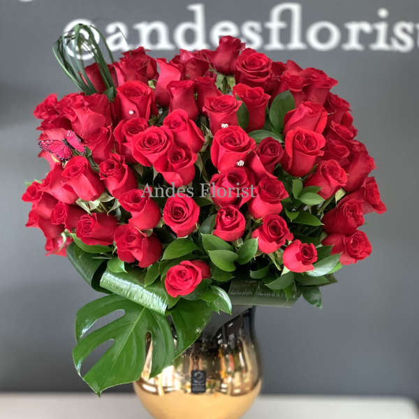 Red rose bouquet in a gold vase with large green leaves