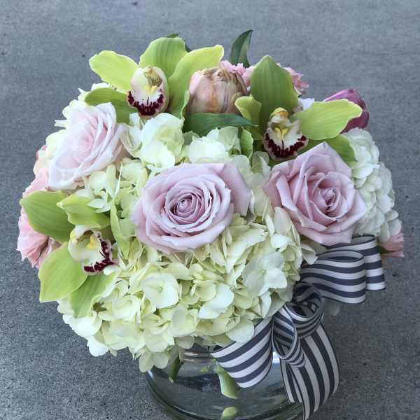 Bouquet of pale pink roses, hydrangeas, and green orchids in a glass vase