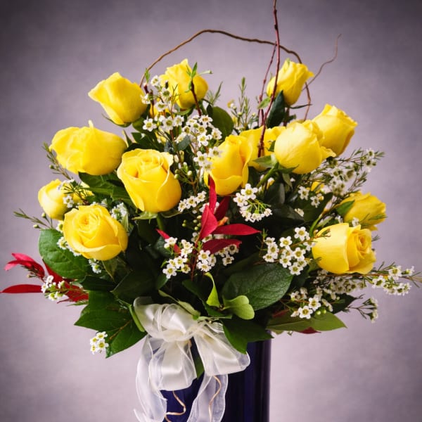 Yellow roses arranged in a tall blue vase with a white ribbon bow