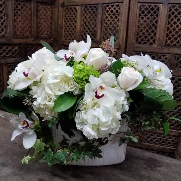 White floral arrangement in a white container with orchids and roses